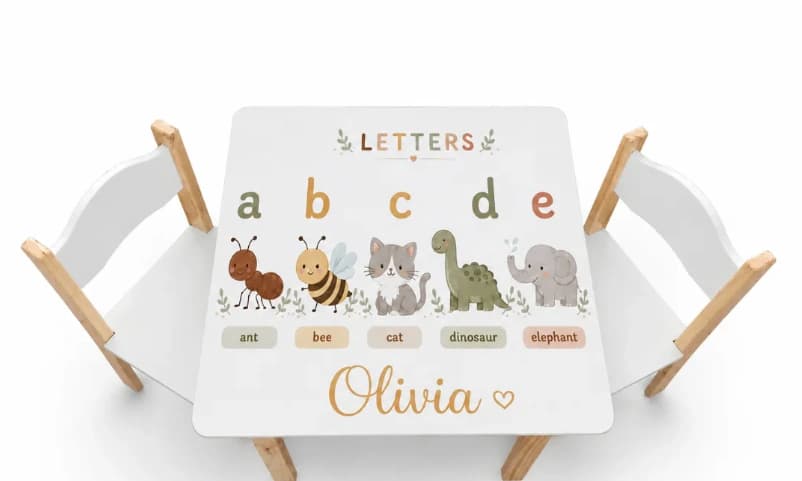 Mesa infantil con un abecedario en inglés ilustrado con animales y el nombre Olivia, con dos sillas blancas